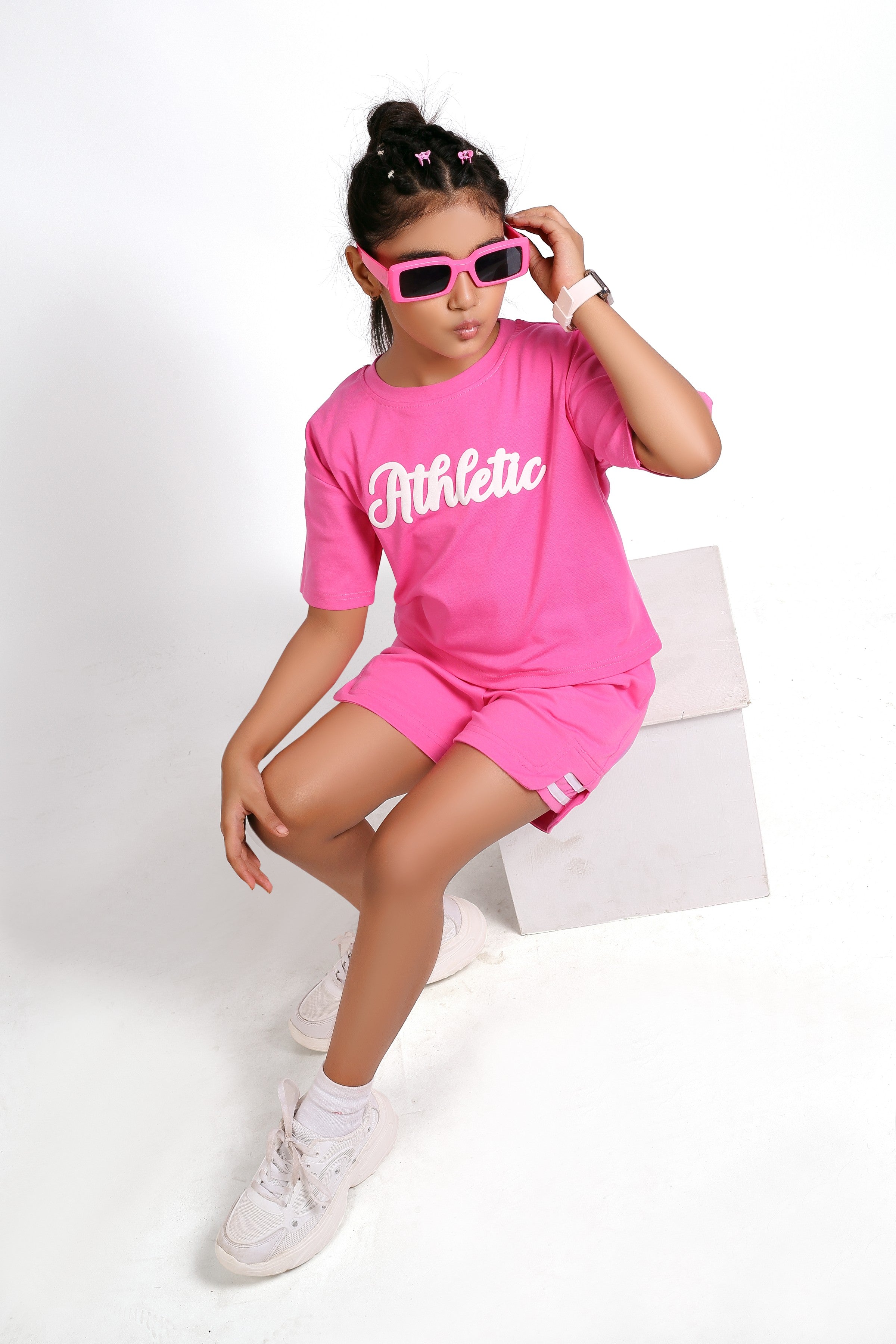 Person wearing a pink 'Athletic' outfit with sunglasses and white sneakers on a white background