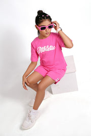 Person wearing a pink 'Athletic' outfit with sunglasses and white sneakers on a white background